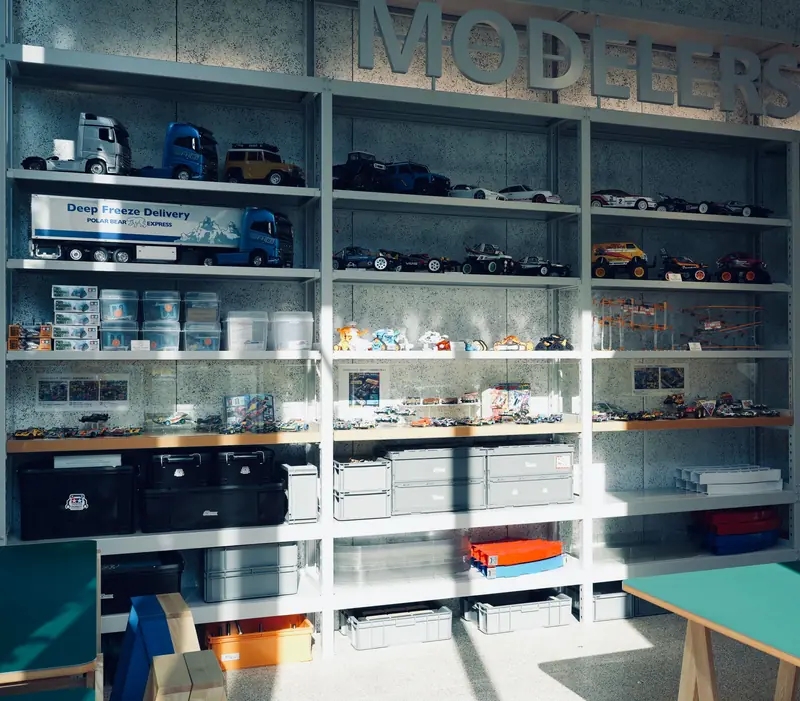 A collection of model cars and storage containers organized on metal shelves in a well-lit room