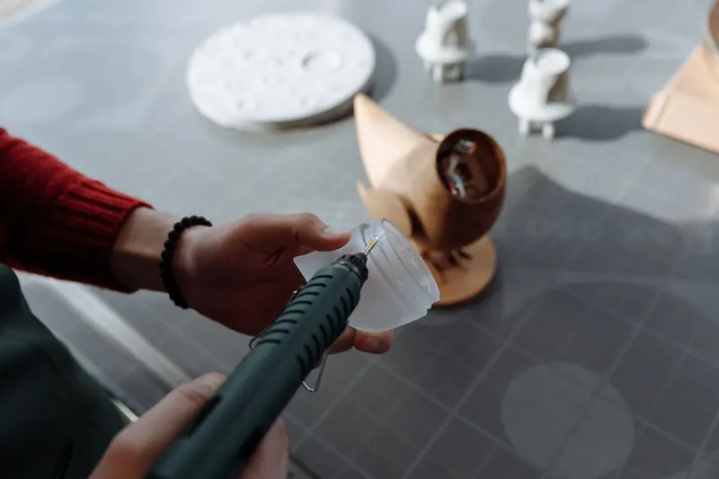 Close-up of hands using a glue gun in a workshop setting, crafting a wooden figurine