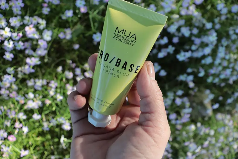 Close-up of a hand holding a makeup primer tube with flowers in the background, perfect for cosmetics brands