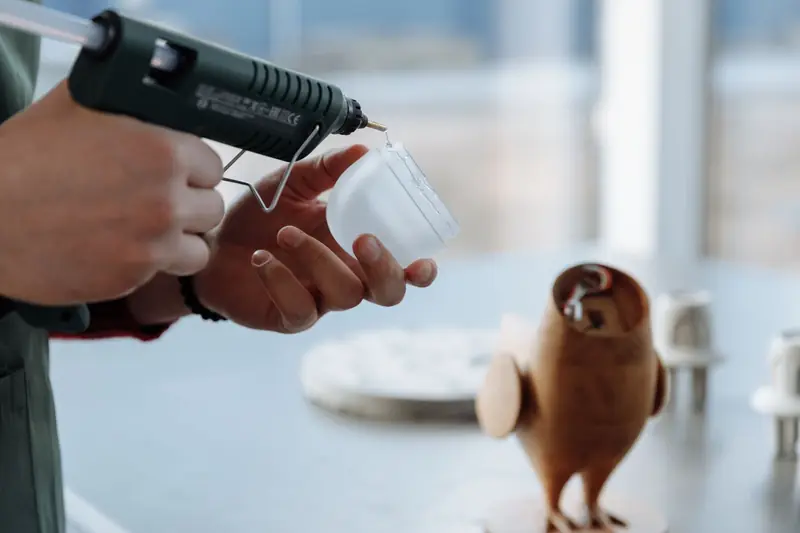 Close-up of hands using a glue gun to craft a wooden figurine in a workshop setting