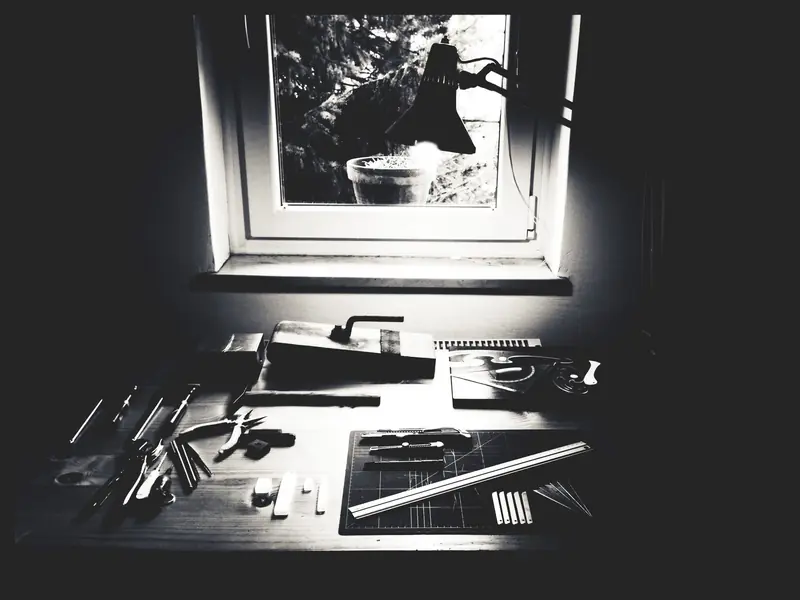 Monochrome workbench setup with crafting tools and equipment near a window