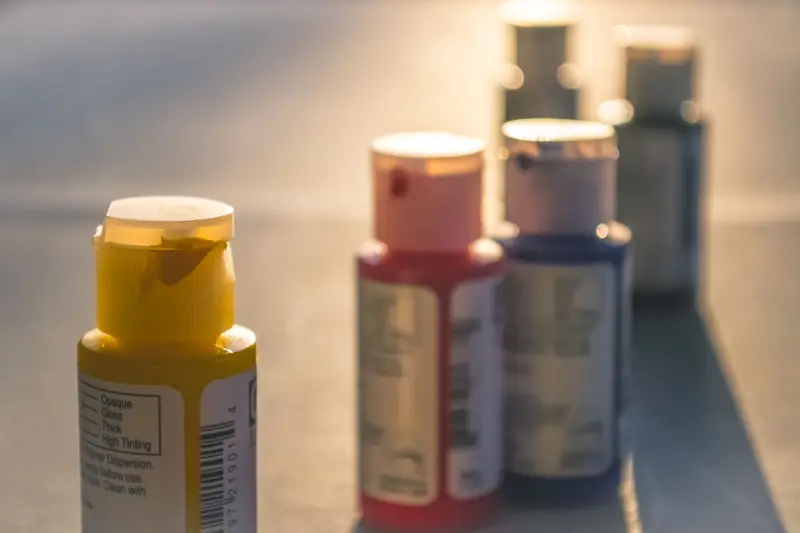 Close-up view of acrylic paint bottles in sunlight, highlighting vibrant primary colors